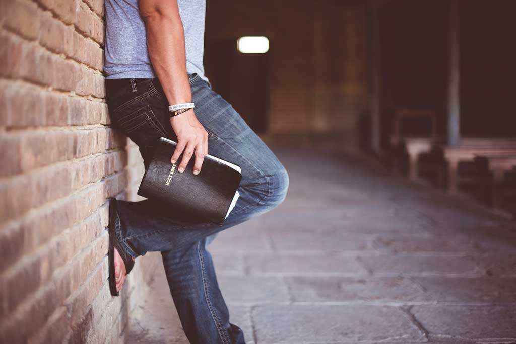 Man standing up against wall with Bible