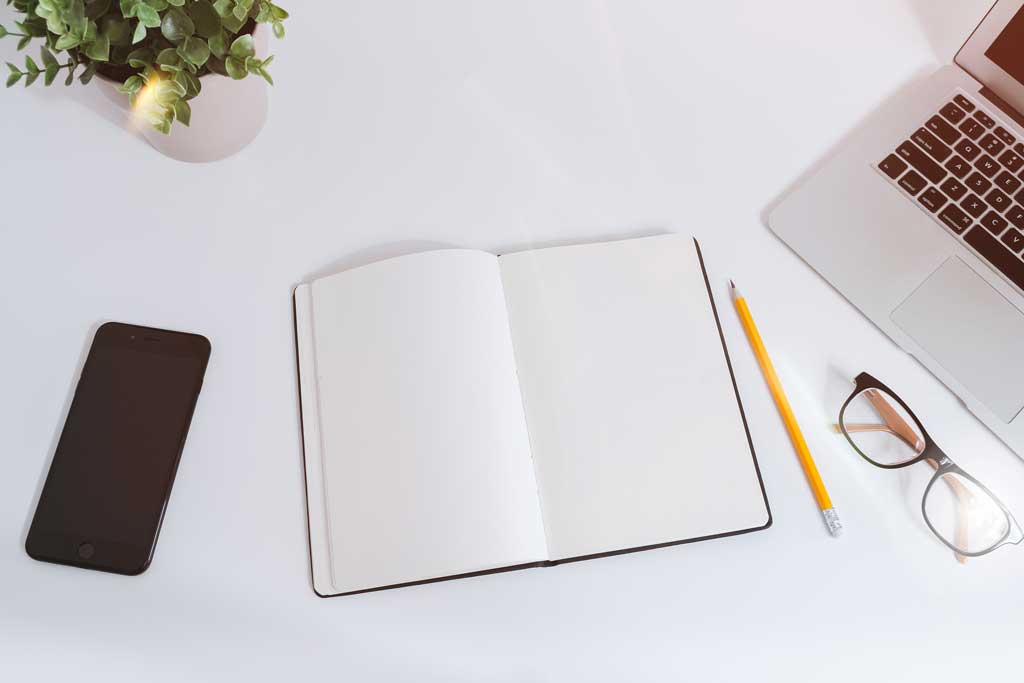 Eco-friendly notebook on a desk with phone, plant, pencil, glasses, and laptop.