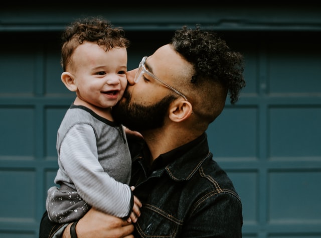 Father holding and kissing smiling baby boy with matching haircut