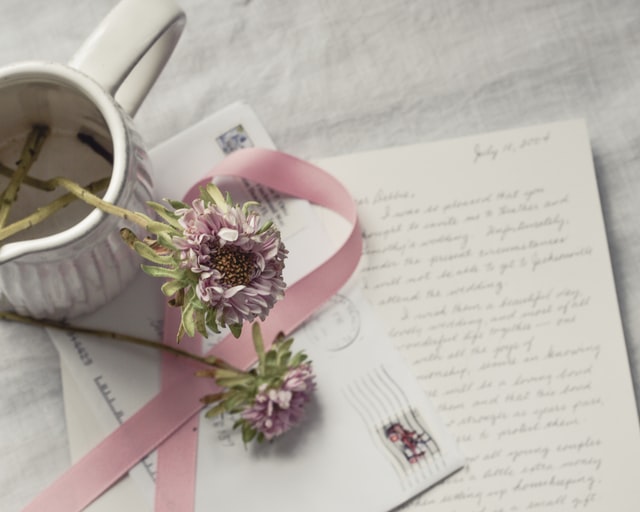 Handwritten letter and postmarked envelope from pen pal, plus flowers and ribbon on table with tablecloth