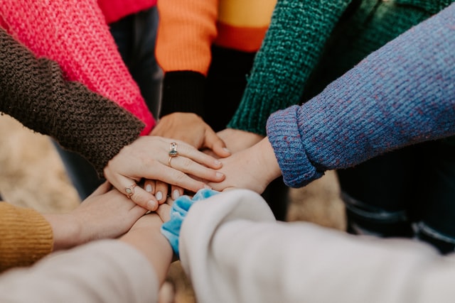Employee team building outdoor event showing employees in bright sweaters stacking hands