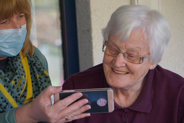 Older person with healthcare professional looking together at smartphone in senior care facility