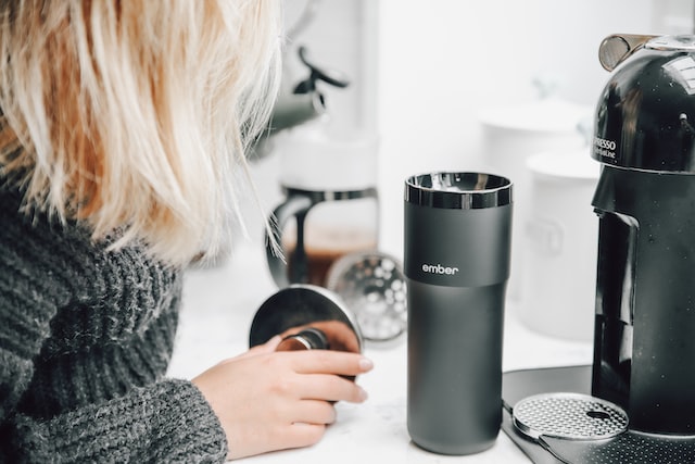 Person wearing sweater and filling customized tumbler with morning coffee