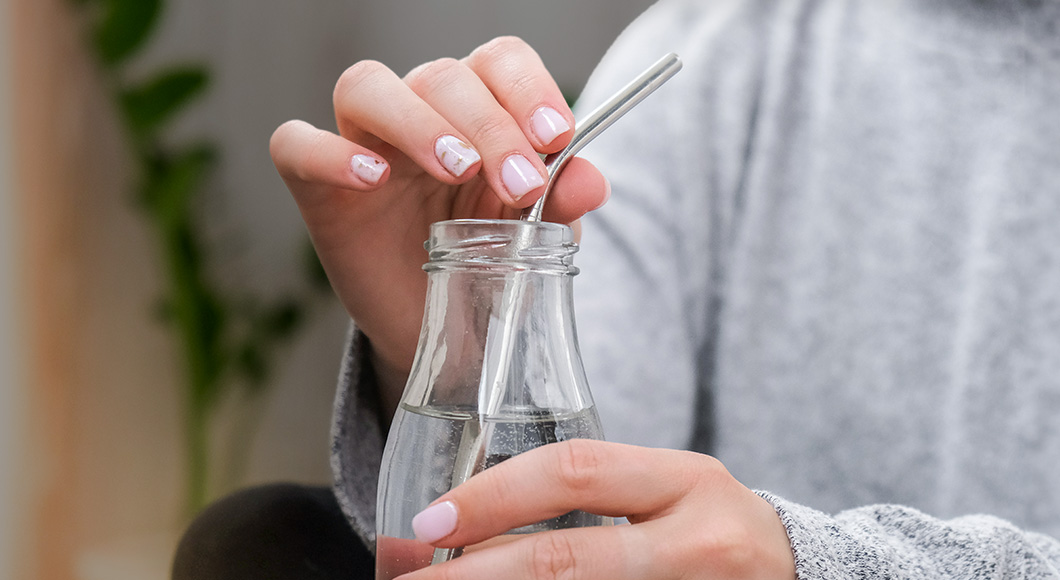 Customer using a stainless steel reusable straw in a glass bottle.