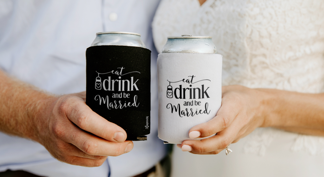 just-married couple holding custom wedding Koozie® can coolers that say "eat, drink, and be married."