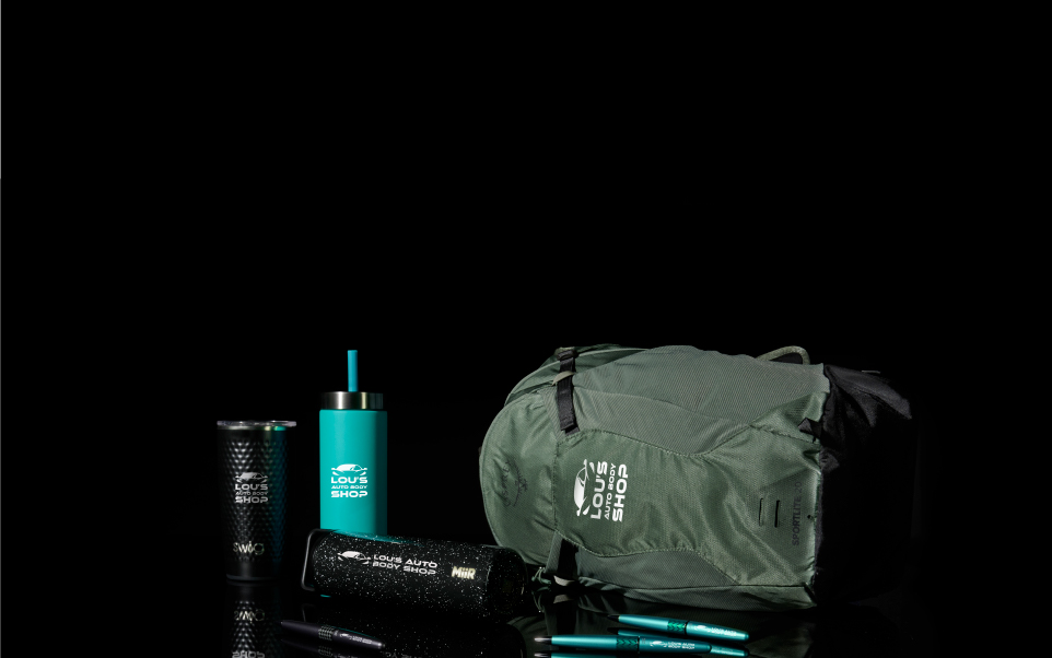 Display banner for promotional products related to the car and automotive industry.  Black water bottles, tumblers, a torquoise water bottle and green backpack printed with a white auto shop logo are featured against a black background.