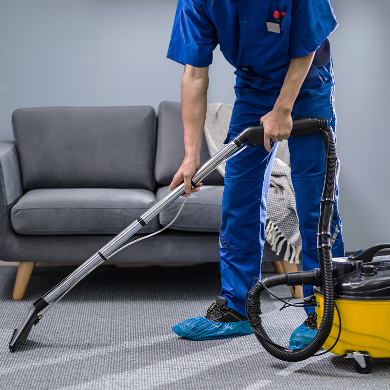 A person dressed in work clothes vacuuming a carpet