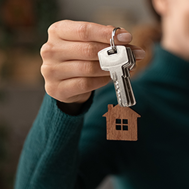 Eine Hand, die einen Schlüssel mit einem Schlüsselanhänger in Form eines Hauses hält