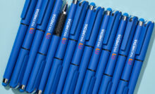 Leuchtend blaue Kugelschreiber mit Logo, Kappe und Stylus auf hellblauem Tisch